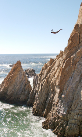 Extreme Cliff Diving: A man cliff dives from a large cliff by the ocean.